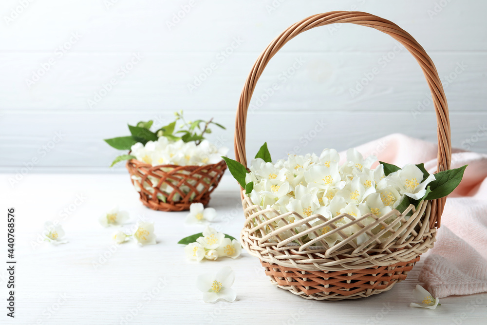 Beautiful jasmine flowers in wicker basket on white wooden table. Space for text