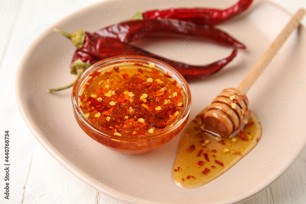 Plate with hot honey and chili peppers on light wooden background, closeup - obrazy, fototapety, plakaty 