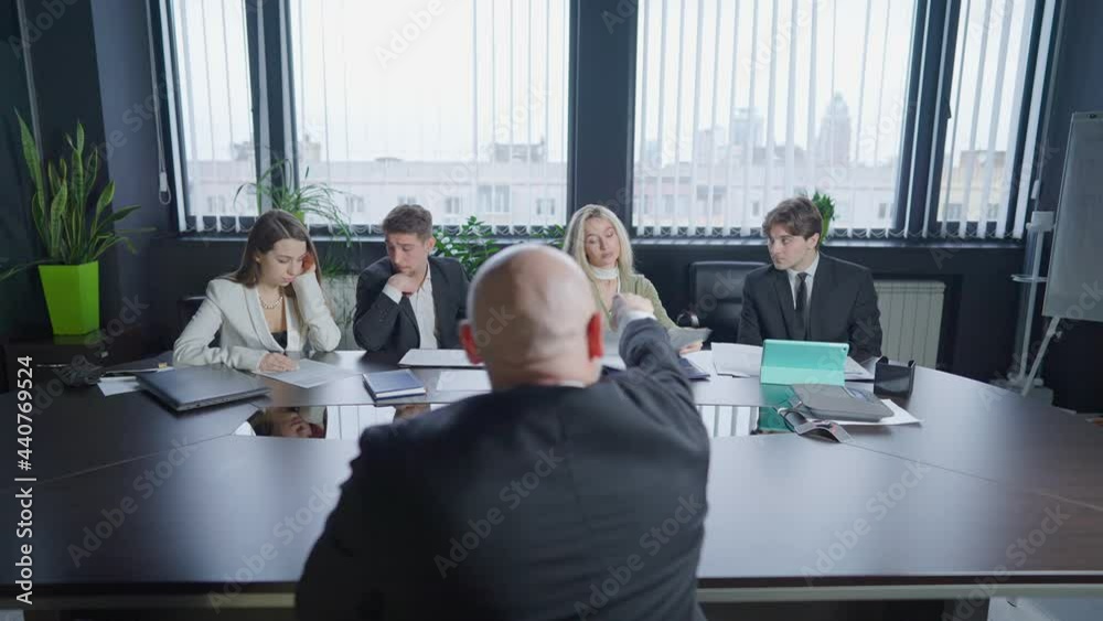 Back view of angry boss yelling and gesturing as group of colleagues sitting at conference table. Male Caucasian manager scolding office staff as woman leaving boardroom. Business conflicts concept Back view of angry boss yelling and gesturing as group of colleagues sitting at conference table. Male Caucasian manager scolding office staff as woman leaving boardroom. Business conflicts concept