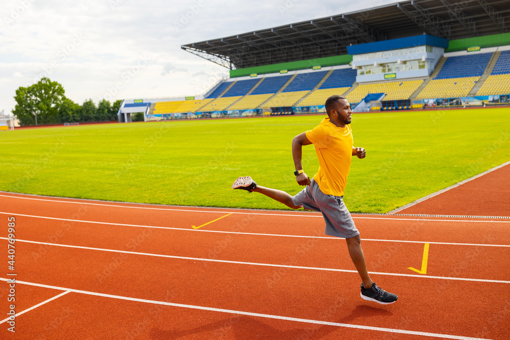 Fototapeta premium Joyful energetic African American sportsman athlete in yellow sportswear running at the stadium, preparing for competition, working hard to win the competitors