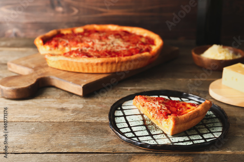Board with tasty Chicago-style pizza and cheese on wooden background