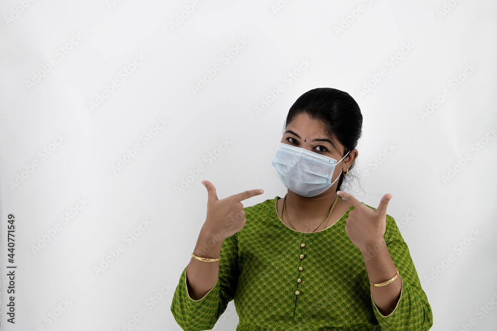 Beautiful smiling Indian young woman in protective face mask, happy female in medical facial cover from COVID-19 thinking, healthcare concept, isolated over white background with space at left Beautiful smiling Indian young woman in protective face mask, happy female in medical facial cover from COVID-19 thinking, healthcare concept, isolated over white background with space at left
