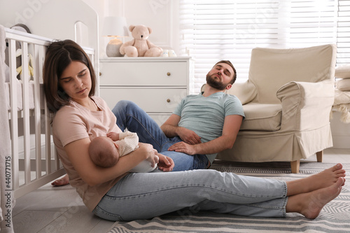 Tired young parents with their baby sleeping on floor in children's room photo