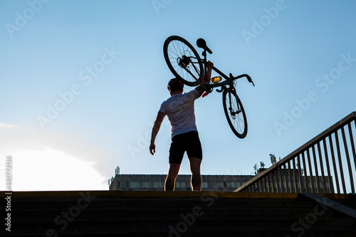 Rear view shot of a muscular cyclist holding up his bicycle in the air, celebrating successful competition