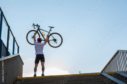 Rear view full length shot of an athletic man lifting his bicycle in the air over his head, copy space