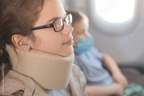 A teenage girl wearing a support collar on her neck on board an airplane. The concept of a comfortable traveling, unloading of the cervical spine, a device for sleeping in flight.