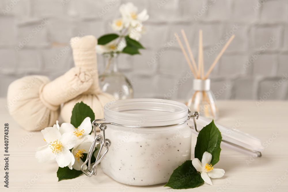 Jar of salt scrub and beautiful jasmine flowers on white wooden table Jar of salt scrub and beautiful jasmine flowers on white wooden table