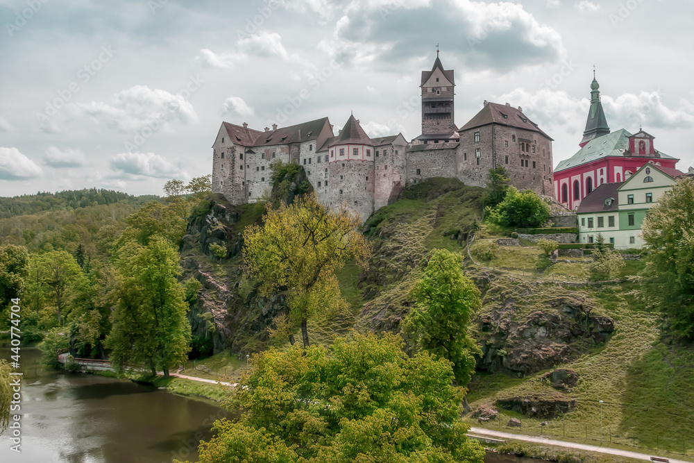 Древняя крепость Локет в Чехии летом. Средневековый замок - главная городская достопримечательность расположен на высокой скале в окружении реки и вековых деревьев. Серо-голубое небо с облаками 