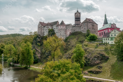 Древняя крепость Локет в Чехии летом. Средневековый замок - главная городская достопримечательность расположен на высокой скале в окружении реки и вековых деревьев. Серо-голубое небо с облаками 