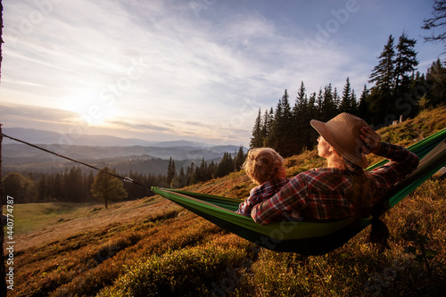 Boy with mom resting in a hammock in the mountains at sunset
