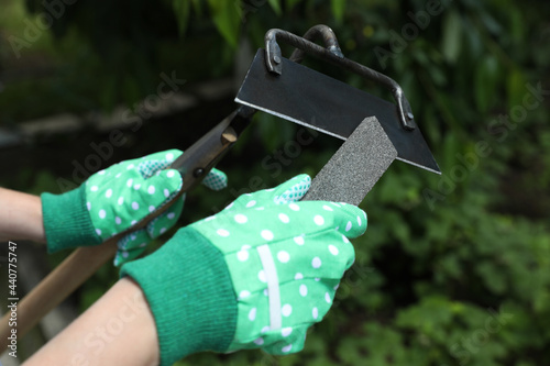 Woman sharpening hoe outdoors, closeup. Gardening tools