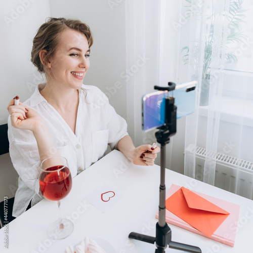 A woman who has a video call on her smartphone draws a greeting card with a heart. Remote acquaintance or declaration of love during quarantine. Virtual Valentine's Day.medium shot