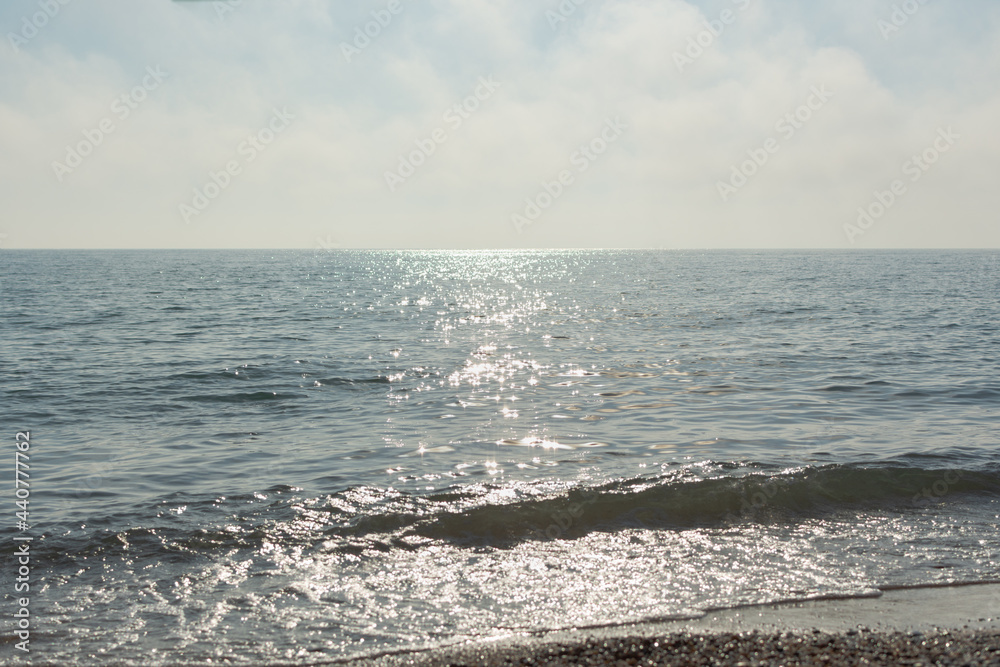 Silver sea glittering background. Minimalistic summer landscape in shades of gray and silver. Midday hot day. The bright sun is reflected in the waves. Natural horizontal background with copy space