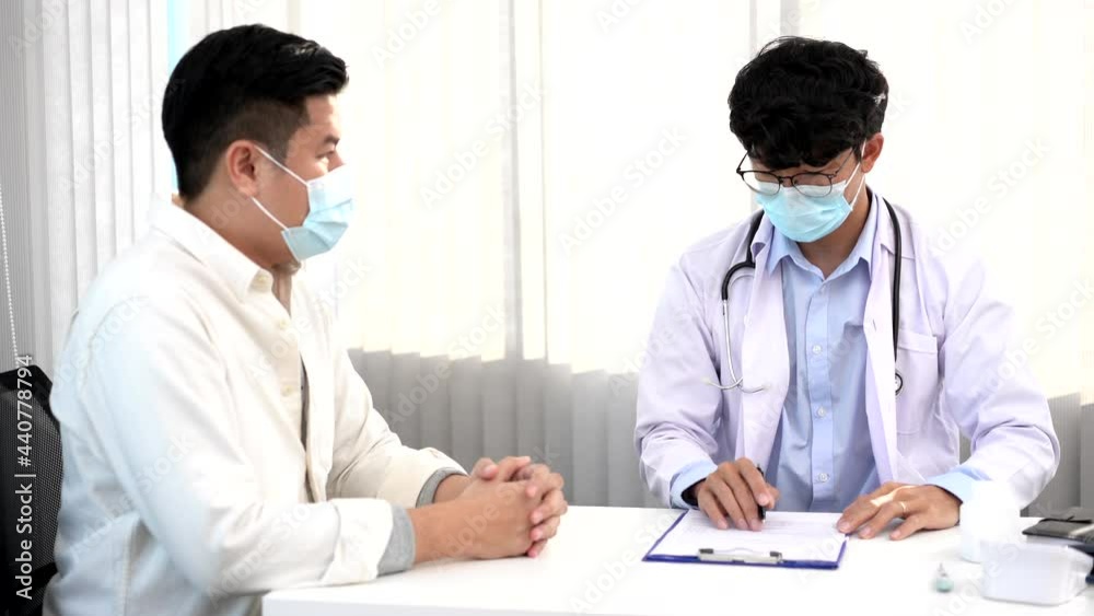 Medical concept a smart male doctor wearing a mask consulting with patient about how to recover from Coronavirus outbreak (COVID-19) at his modern clinic. Medical concept a smart male doctor wearing a mask consulting with patient about how to recover from Coronavirus outbreak (COVID-19) at his modern clinic.