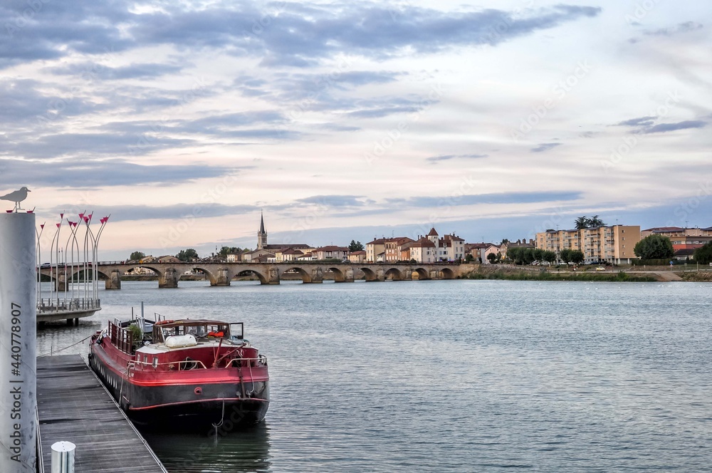 Nice view of a boat in the river Saône and the Saint-Laurent bridge, which connects the center of Macon and the other bank where the town of Saint Laurent offers many restaurants