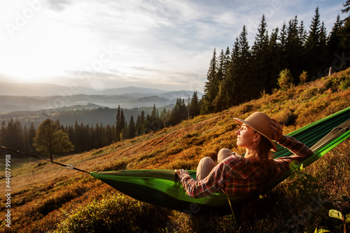 Woman hiker resting after climbing in a hammock at sunset