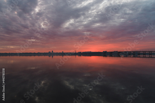 Beautiful sunset sky in the city. Sunrise or sunset. Dnepr River. The sky is reflected in a quiet river. Photo from Drona