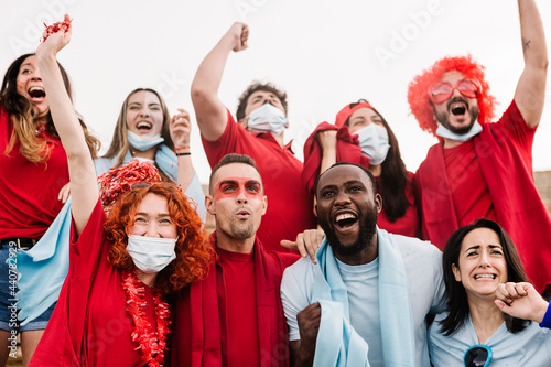 Multiracial sports fans in protective face masks screaming while supporting their team at stadium -  Coronavirus spread prevention  and live sports new normality concept photo
