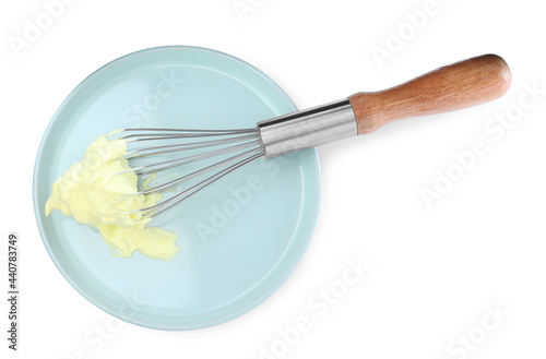 Balloon whisk with yellow cream and plate isolated on white, top view
