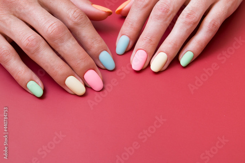 Colored matte manicure on female hands on a red background with copy space