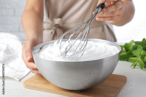Canvas Print Woman whipping white cream with balloon whisk at wooden table, closeup