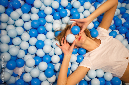 Young woman play with white and blue balls in a dry pool