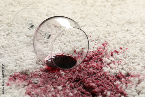 Overturned glass and spilled red wine on white carpet, closeup