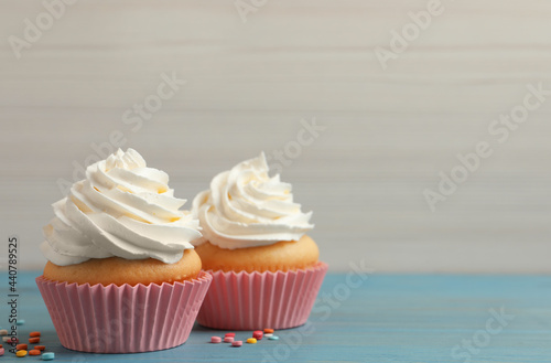 Delicious cupcakes decorated with cream on light blue wooden table, space for text