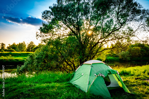 green tourist tent by the river at sunset