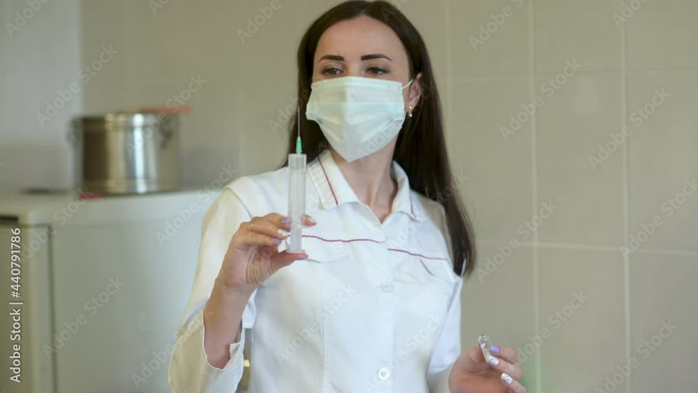 Female Doctor in medical Uniform and protective face mask holds a syringe and vaccine bottle at the hospital. Health and medical concepts.