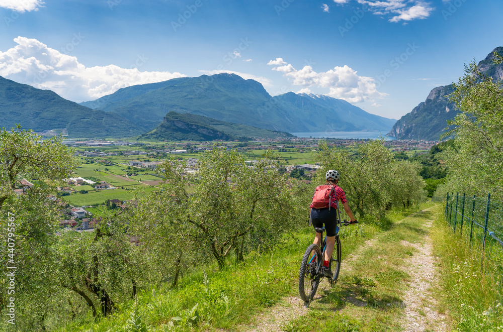 nice senior woman riding her  electric mountain bike in the olive groves of Arco and enjoying the awesome view over Garda Lake between Riva del Garda and Torbole