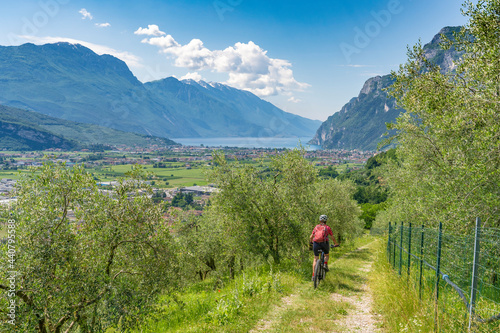 nice senior woman riding her electric mountain bike in the olive groves of Arco and enjoying the awesome view over Garda Lake between Riva del Garda and Torbole
