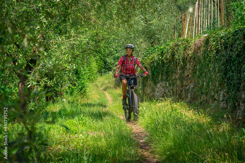 nice and active senior woman riding her electric mountain bike in the Garda lake mountains between blooming the olive groves of Arco close to Riva del Garda and Garda Lake , Landscape © Uwe