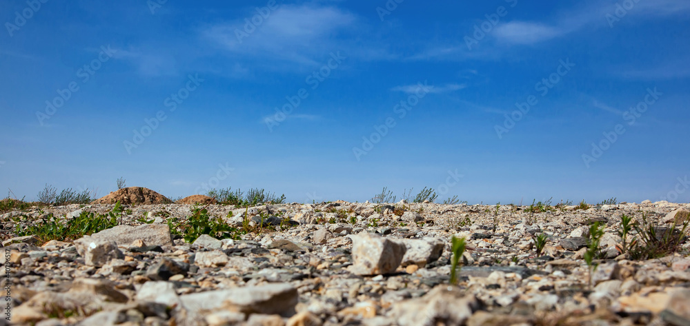 Panorama of desert rocky land and blue sky. Stony soil with sparse vegetation. Bottom view. Industrial dumps.