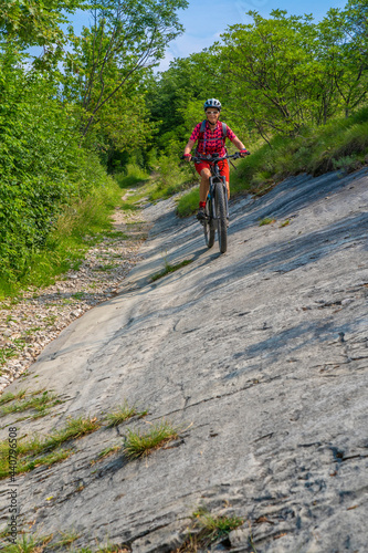 nice, active senior woman riding her electric mountain bike in the huge rock fall area of Marocche di Dro, in the Sarca Valley, Garda lake mountains, Trentino, Italy 