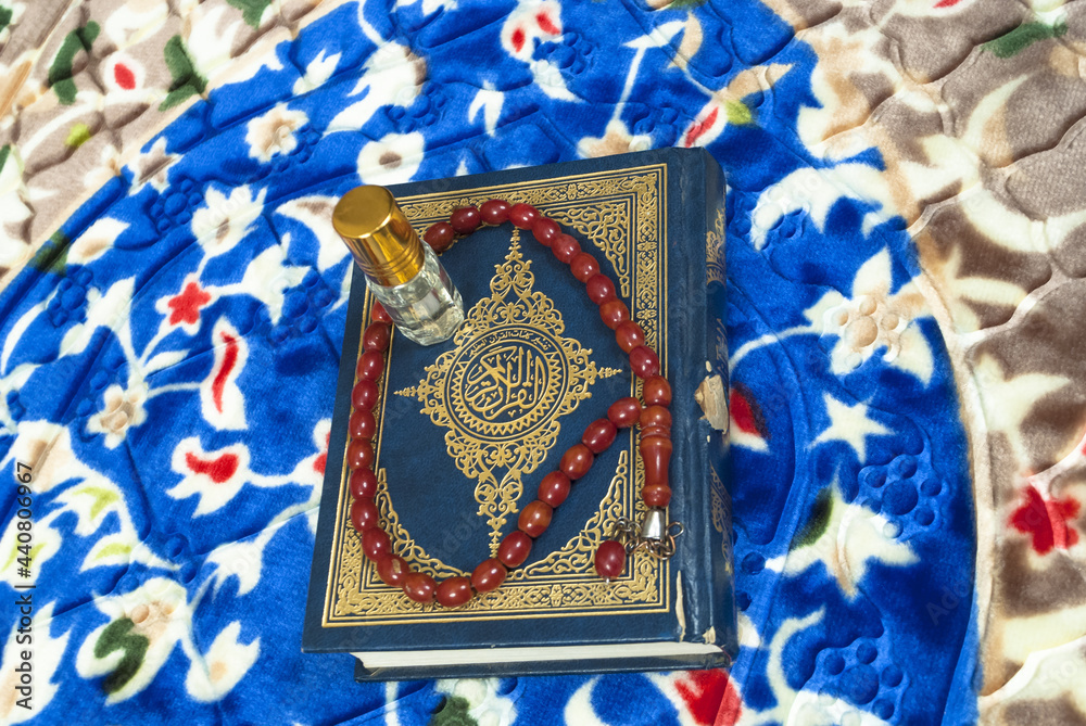 Islamic book holy Quran with rosary beads and scent bottle on colorful prayer mat,Muslim religious