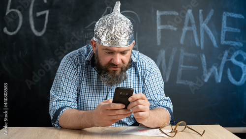 Fényképezés portrait of a crazy conspiracy theorist with a mobile phone in his hands and a protective cap made of foil is of electric waves and radiation