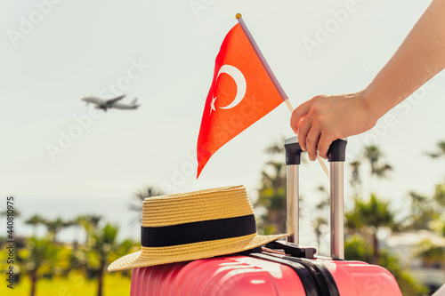 Fototapeta Naklejka Na Ścianę i Meble -  Woman with pink suitcase, hat and Turkey flag standing on passengers ladder and getting out of airplane opposite sea coastline with palm trees.
