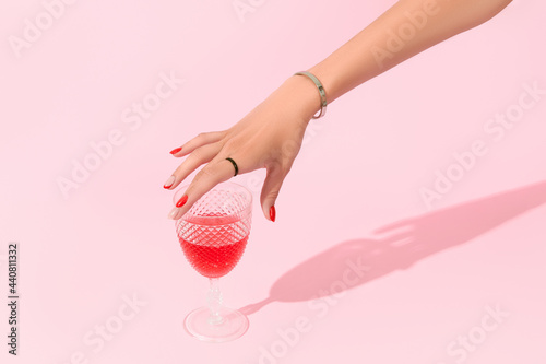 Womans hand holding glass on pink background. Manicure design trends photo