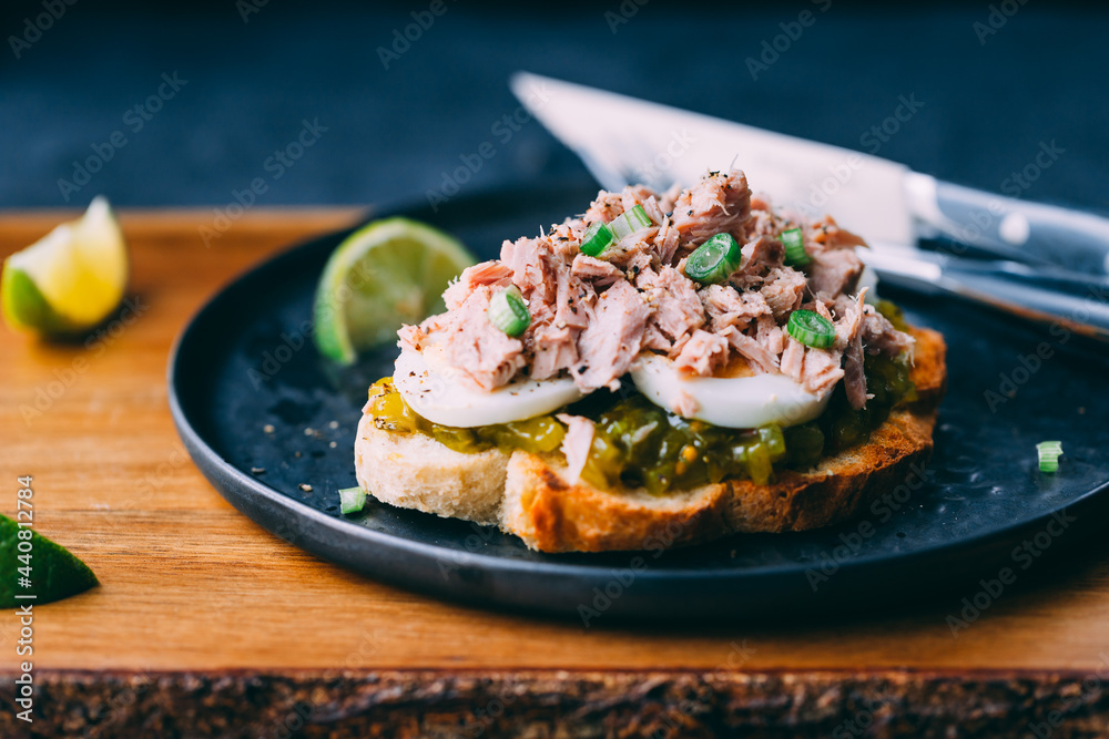 Open sandwich with canned tuna, egg and pickled cucumber dressing served with lime. Open sandwich with canned tuna, egg and pickled cucumber dressing served with lime.