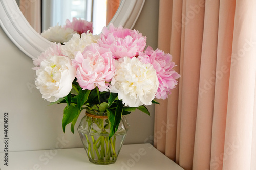 Studio shot of beautiful peony flowers in a glass vase on a table over gray wall background with a lot of copy space for text. Feminine floral composition. Close up, backdrop.