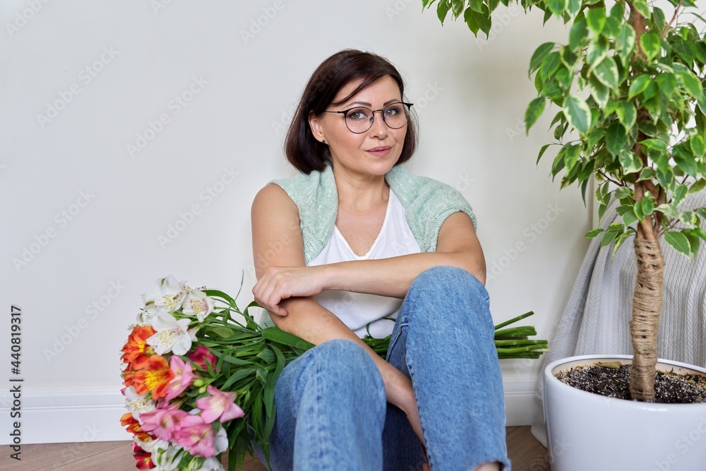 Smiling middle aged woman with bouquet of flowers sitting on the floor at home Smiling middle aged woman with bouquet of flowers sitting on the floor at home