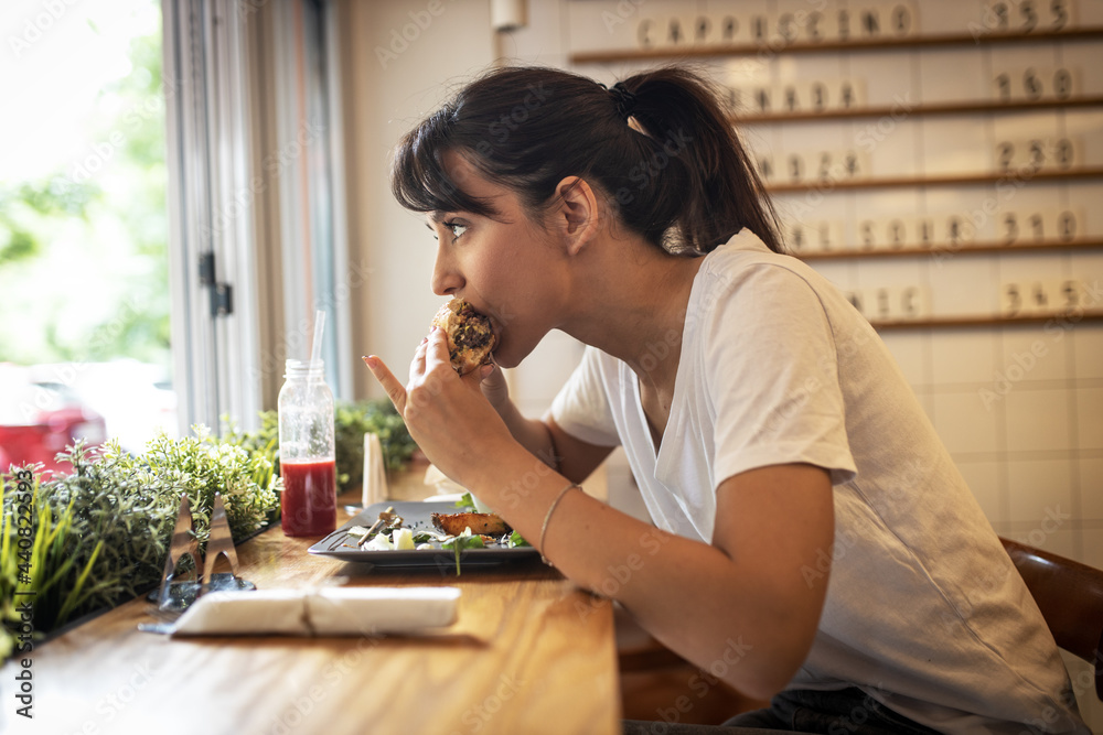 Teenage girl sitting in fast food restaurant eating burger and drinks fresh organic juice.	
