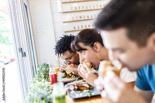 Young people sitting in street fast food restaurant and eating burgers. 