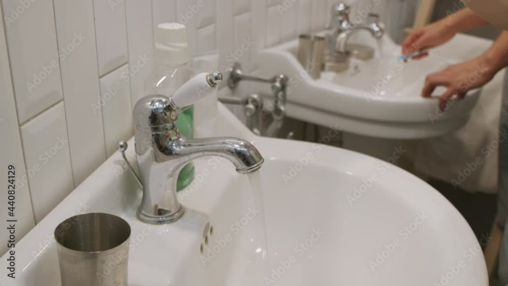 Handheld close up shot of unrecognizable men wetting their toothbrushes in bathroom while brushing teeth Handheld close up shot of unrecognizable men wetting their toothbrushes in bathroom while brushing teeth