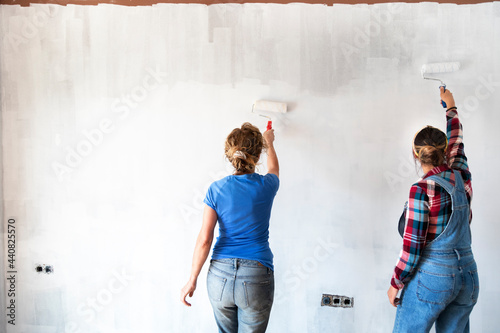 Two women painting new apartment walls in color white with paint roller. Renovating home. © Daniel