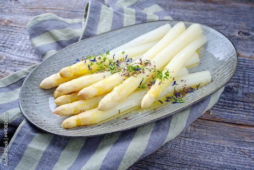 Modern style traditional steamed white asparagus garnished with butter sauce and herbs served as close-up on a design plate