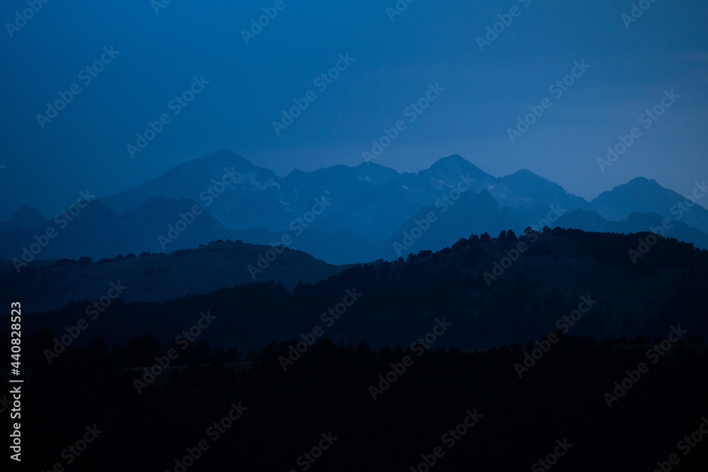 Mountains layers during blue hour. Landscape with dark blue misty silhouettes of alpine mountains and fir trees forest in Pyrenees.