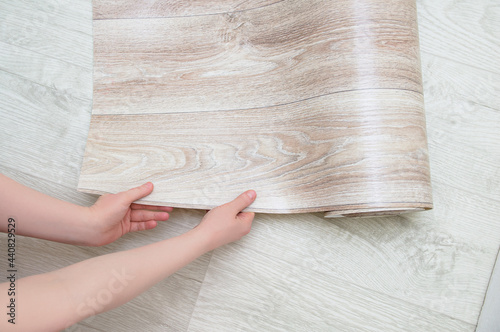 Laying beige linoleum with wood texture on white wooden floor.