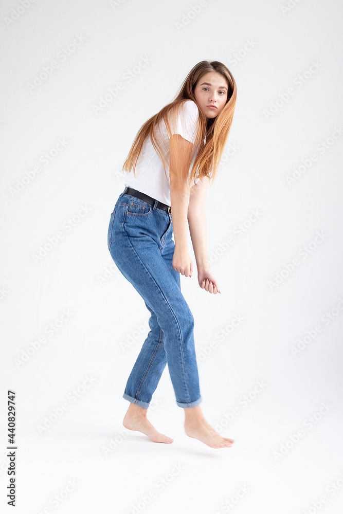 young attractive caucasian woman with long hair in t-shirt and blue jeans dances on white studio background. skinny pretty female dancing on cyclorama with bare feet. model tests of beautiful lady young attractive caucasian woman with long hair in t-shirt and blue jeans dances on white studio background. skinny pretty female dancing on cyclorama with bare feet. model tests of beautiful lady